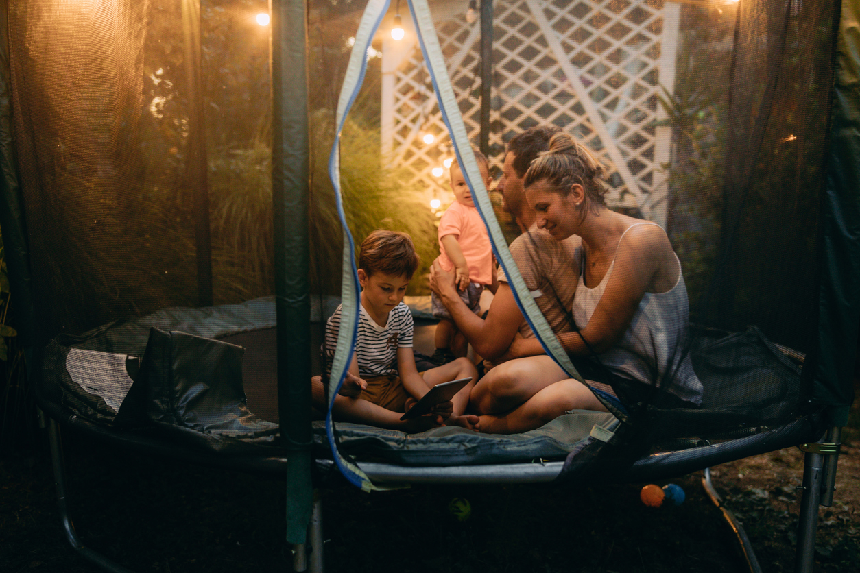 Ein Familie sitzt mit mit einem Tablet auf dem Trampolin