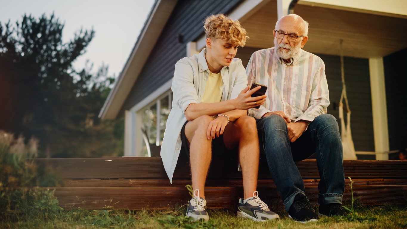 Ein Junge und ein älterer Mann sitzen mit einem Smartphone auf der Veranda