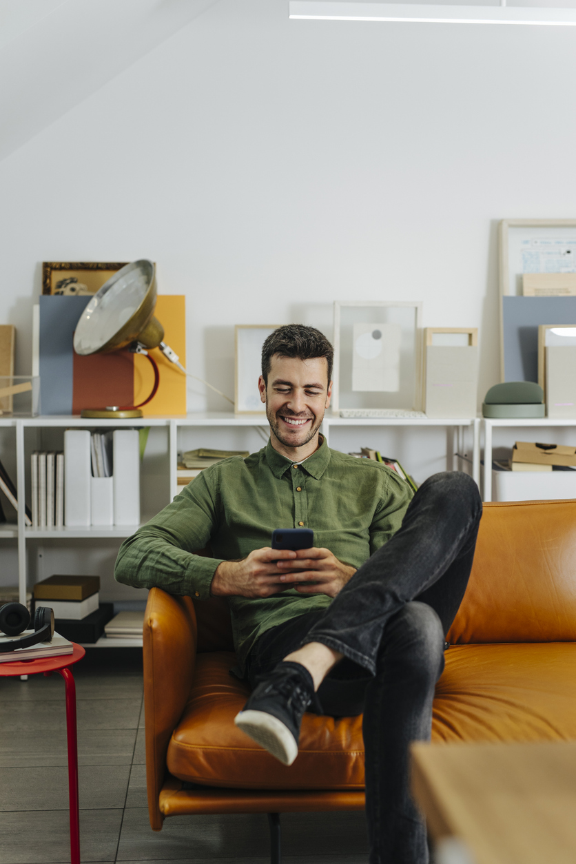 Ein Mann sitzt mit Smartphone auf einer Couch