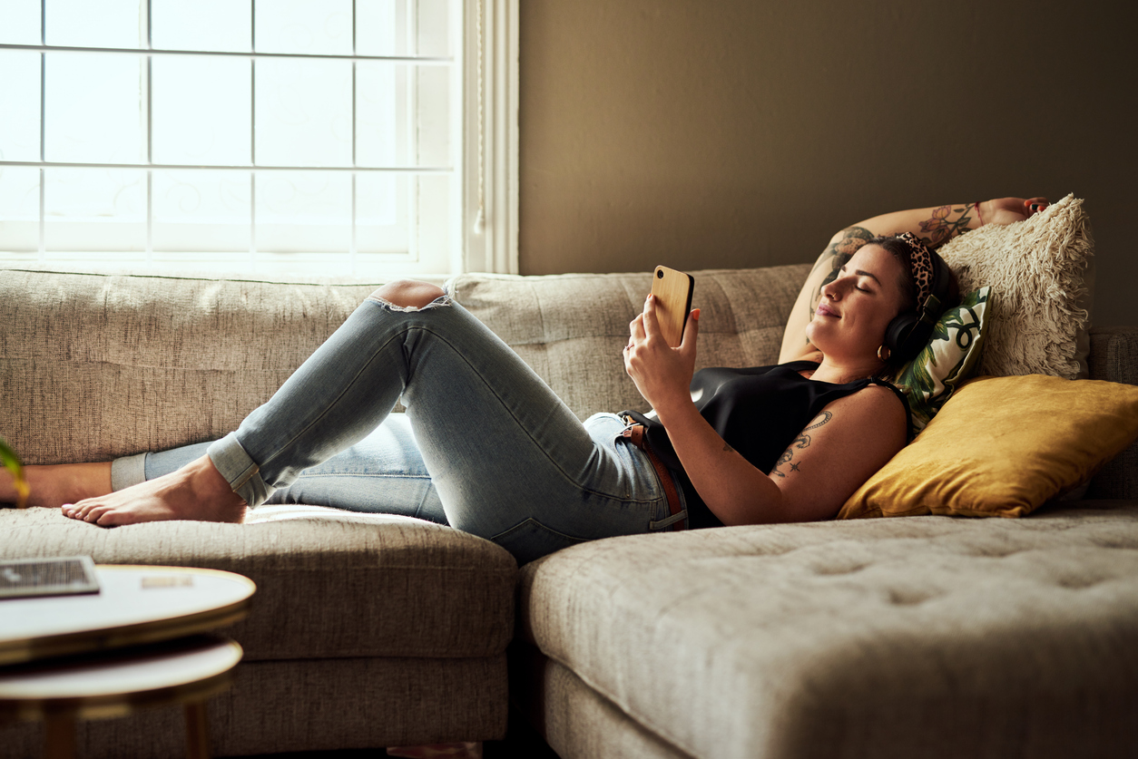 Frau liegt mit Smartphone auf der Couch